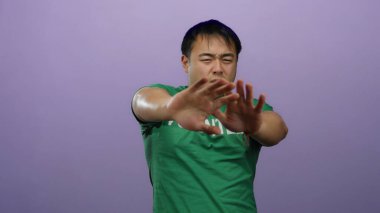 Yeşil gönüllü gömlekli genç adam mor arka planda şakacı hareketler yapıyor.