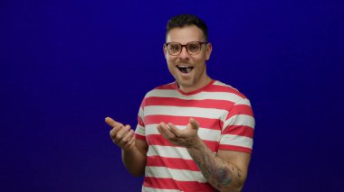 Mavi arka planda, çizgili gömlek ve gözlük takan genç adam, canlı kontrastı ve gündelik tarzı vurguluyor..