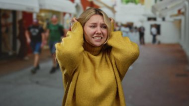 Şehir sokaklarında hayal kırıklığına uğramış sarı kazak giyen, sarı saçlı ve gergin yüzlü bir kadın. Kalabalık şehir ortamında strese maruz kalıyor..