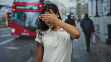 Meşgul şehir caddesinde arka planda ikonik kırmızı otobüsle el ele duran kadın, şehir hayatını ve anonimliği simgeliyor..