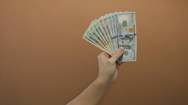 Amerikan banknotlarını fan şeklinde sergileyen beyaz bir adamın olduğu kahverengi bir arka planda bize dolar uzattı..