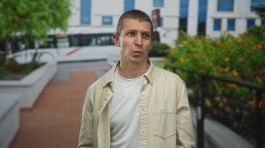 Şehir caddesinde duygularını ifade eden bir adam yeşil yapraklı ve arka planda modern binalar açık şehir manzarasını gösteriyor..