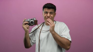 Elinde pembe arka planda neşeli bir ifadeyle klasik kamera tutan genç bir adam..