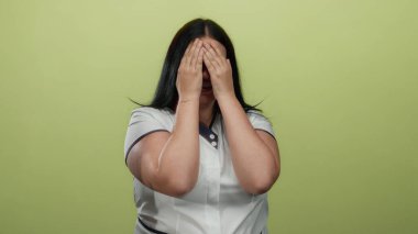 Genç ve cüsseli bir kadın, neşeli bir şekilde gülümseyerek yüzünü örtüyor ve canlı sarı bir arka plana karşı, neşeli bir şekilde güven ve neşe saçıyor..