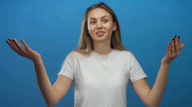 İzole edilmiş mavi arka plana karşı beyaz gömlekle gülümseyen genç ve anlamlı duygular taşıyan kadın jestleri.