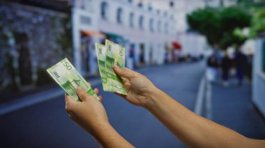 Kentsel bir açık hava ortamında Norveçli kron banknotları tutan eller, şehir sokaklarında iş ve yatırım faaliyetleri izlenimi uyandırıyor.