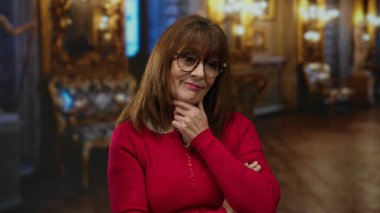 Kadın gözlük ve kırmızı süveter giyerken süslü müze ortamında düşünür düşünceli ve düşünceli bir atmosfer yaratır..