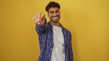 Kameraya bakan genç adam, parlak sarı bir arkaplana güvenle gülümsüyor. Günlük kıyafetler giyiyor. Mutlu ve cana yakın görünüyor..