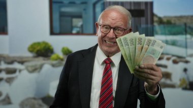 Czech Koruna banknotlarını elinde tutan kıdemli bir adam bir sokakta, iş başarısını gösterirken kendine güvenen bir ifadeyle.