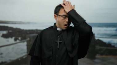 Rahip kılığındaki bir adam okyanus manzarasıyla duygularını ifade ederek deniz kenarında geziniyor..