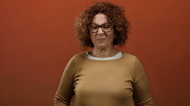 Kıvırcık saçlı İspanyol orta yaşlı kadın, kahverengi arka plandaki kötü kokuya garip bir yüz ifadesi veriyor..