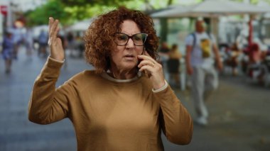 Şehirli sokak ortamında telefonla konuşurken duygusal hareketler yapan bir kadın, hayal kırıklığını ya da sohbete olan bağlılığını gösteriyor.