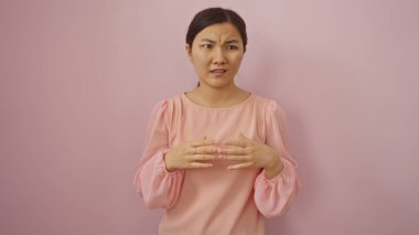 Pembe bluzlu kadın soyutlanmış pembe arka planda duruyor. Elleri hareketli düşünceli görünüyor.