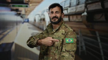 Omzunda Brezilya bayrağı olan askeri üniformalı bir adam yolcu gemisinin güvertesinde durmuş parlak ışığın altında bayrağı doğrultuyor..