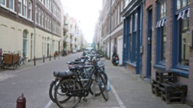 Bisikletler, Amsterdam, Hollanda 'da bulanık tuğla binalar ve bulanık bir arka planla şehrin kentsel mimarisini ve cazibesini gözler önüne seren odak dışı bir caddenin yanında dizildi..