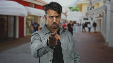 Genç İspanyol bir adam hareketli bir şehir caddesinde jest yapıyor, kamerayı kendinden emin bir ifadeyle davet ediyor, şehir manzarası ile çevrili ve yoldan geçenleri bulanıklaştırıyor..