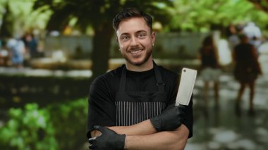 Parkta bıçaklı ve eldivenli önlük giymiş gülümseyen genç bir adam, açık havada neşeli bir kasabı somutlaştırıyor..