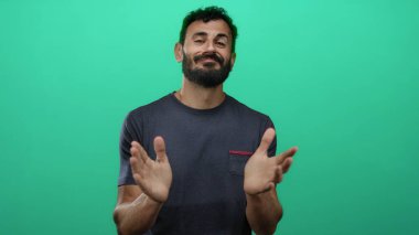 Sakallı İspanyol bir adam canlı yeşil arka planda el çırpıyor, günlük tişört giyiyor, stüdyo ortamında pozitiflik ve dostluk iletiyor..