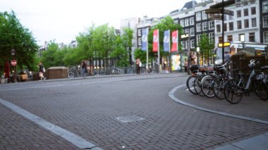 Amsterdam 'da bulanık bir sokak sahnesinde bulanık insanlar bulutlu bir günde geleneksel Hollanda mimarisinin arka planına parketmiş yürüyorlar ve bisikletler sürüyorlar..