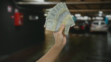 Kapalı otoparkta Endonezya paralarını elinde tutan beyaz bir adam modern bir şehir ortamında para ve finansmanı ön plana çıkarıyor..