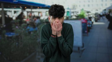 Restoran terasında elleri soğuk sokakta birbirine yapışmış genç bir adam süveter giymiş rahatsız görünüyor..