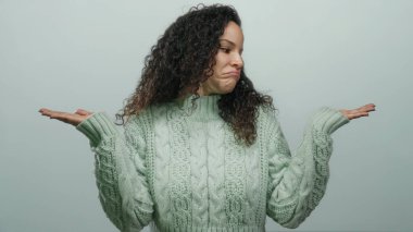 Yeşil kazaklı bir kadın, kollarını aralayıp beyaz arka planda izole edilmiş bir şekilde omuz silkiyor. Stüdyoda belirsizlik duygusunu gündelik tarzda ve İspanyol kökenli bir şekilde aktarıyor.