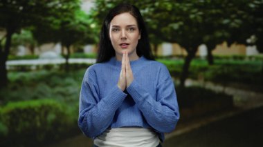 Huzurlu yeşil bir park ortamında meditasyon yapan, açık havada mavi bir kazak giyen, sükuneti ve rahatlığı vurgulayan bir kadın.