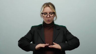 Sakin bir ifadeyle nefes alma egzersizi yapan kadın izole edilmiş beyaz arka planda gözlük takıyor ve siyah takım elbise giyiyor. Elleri birbirinin üstüne nazikçe yerleştirilmiş..