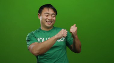 Gönüllü gömlekli genç adam yeşil arka plana gülümsüyor, pozitifliğini ve enerjisini ifade ediyor..
