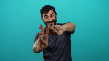 Sakallı İspanyol bir adam, gülümsüyor ve parlak mavi arka plana karşı hashtag işareti yapıyor..