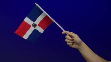 Mavi duvarda Dominik Cumhuriyeti bayrağını taşıyan bir adam vatanseverliğini ve kutlamalarını izole bir ortamda gösteriyor..