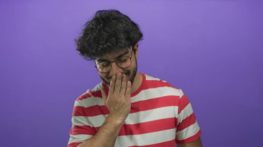 Sakallı ve gözlüklü genç adam kibarca gülümsüyor ve dudaklarını parlak mor bir arka planla örtüyor. Kırmızı çizgili gömleğiyle, eğlence ve samimi bir duyguyu çağrıştırıyor..