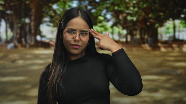 Женщина, держащая за руку пистолет в окружении парка с латиноамериканским и латинским стилем для молодой атмосферы на открытом воздухе среди зеленой листвы во время ношения очков.