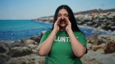 Açık hava etkinliği sırasında güneşli deniz kenarında, sakin sahil manzarası ve kayalık kıyı şeridi ve mavi denizin ortasında gülümseyen gönüllü bir kadın..
