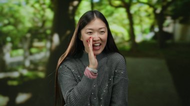 Güneşli bir günde arka planda yeşil ağaçlarla açık hava parkında gülümseyen bir kadın..