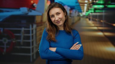 Genç bir kadın, bir yolcu gemisinin güvertesinde kolları bağlı ve renkli gece ışıklarının altında sakin bir ifadeyle rahatlatıcı bir anın tadını çıkarıyor.