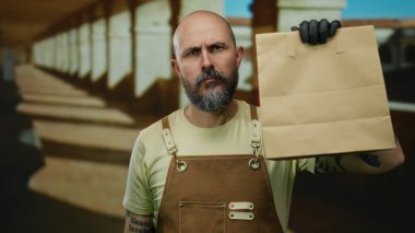 Kahverengi önlüklü kel bir adam eski üniversitede elinde kesekâğıdıyla geziyor. Kemerleri ve kendine güveni olan özel bir eğitim ortamı sergiliyor..