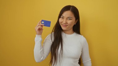 Elinde canlı sarı arka planda, uzun saçlı, beyaz süveter giyen, gülümseyen bir kadın Asya kökenli, kendine güvenen bir kadın, finansal güvenlik konsepti oluşturuyor.