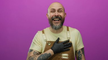 Sakallı kel adam gülüyor ve işaret ediyor. Önlük ve eldiven takıyor. Pembe arka planda..