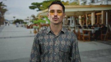 Genç İspanyol adam kalp hareketi yapıyor ve teras caddesindeki bir açık kahve restoranında öpücük yolluyor..