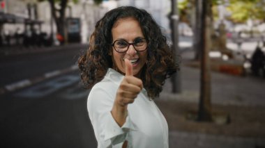 Kıvırcık saçlı, gülümseyen bir kadın şehir sokaklarında olumlu ve kendine güvenen bir kadın..
