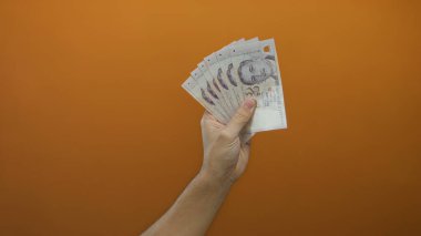 Elinde turuncu bir duvara karşı izole edilmiş, parayla ilgili bir konsept için beyaz bir erkeğe ait banknotlar tutan bir adam..