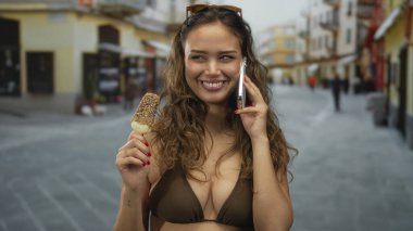 Bikinili İspanyol bir kadın sokakta dikiliyor, akıllı bir telefonla konuşuyor, elinde dondurma tutuyor, gençlik dolu ve canlı bir yaz manzarası yakalıyor..