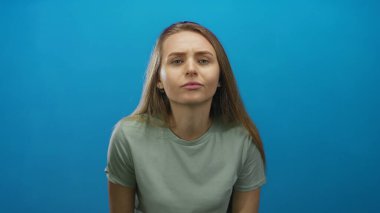 Canlı mavi bir arka plana karşı gelişigüzel giyinmiş bir kadın, izole edilmiş bir stüdyo ortamında merak ve içgözlem duygusu taşıyor..