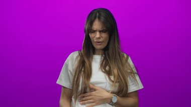 Öksüren ve hapşıran genç İspanyol bir kadın, izole edilmiş mor bir arka planda, günlük beyaz bir gömlek ve kol saati giyiyor, hastalık ve rahatsızlık taşıyor..