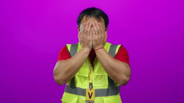 Gönüllü nişanlı sarı yelek giyen Asyalı bir adam tecrit edilmiş pembe bir duvarın karşısında duruyor..