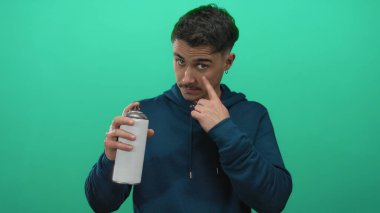 İzole edilmiş yeşil arka plan duvarının üzerinden gözüne işaret eden bir duvar resmi tutan İspanyol genç adam sokak sanatları kültürüne odaklı yaratıcı bir şehir atmosferi yayıyor.