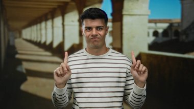 Çizgili süveter giyen genç bir adam tarihi üniversite avlusunda kemerli koridorlar, güneş ışığı altında mizah ile bir araya gelen cazibe.