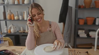 Önlüklü kadın stüdyoda kil ve tekerleği nazikçe şekillendirmek için elleri kullanır; yaratıcılık farkındalığı odak noktası.