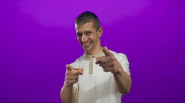 Neşeli adam canlı mor bir arka plana bakıp gülümsüyor, dinamik jestler ve anlamlı duygular yakalıyor..